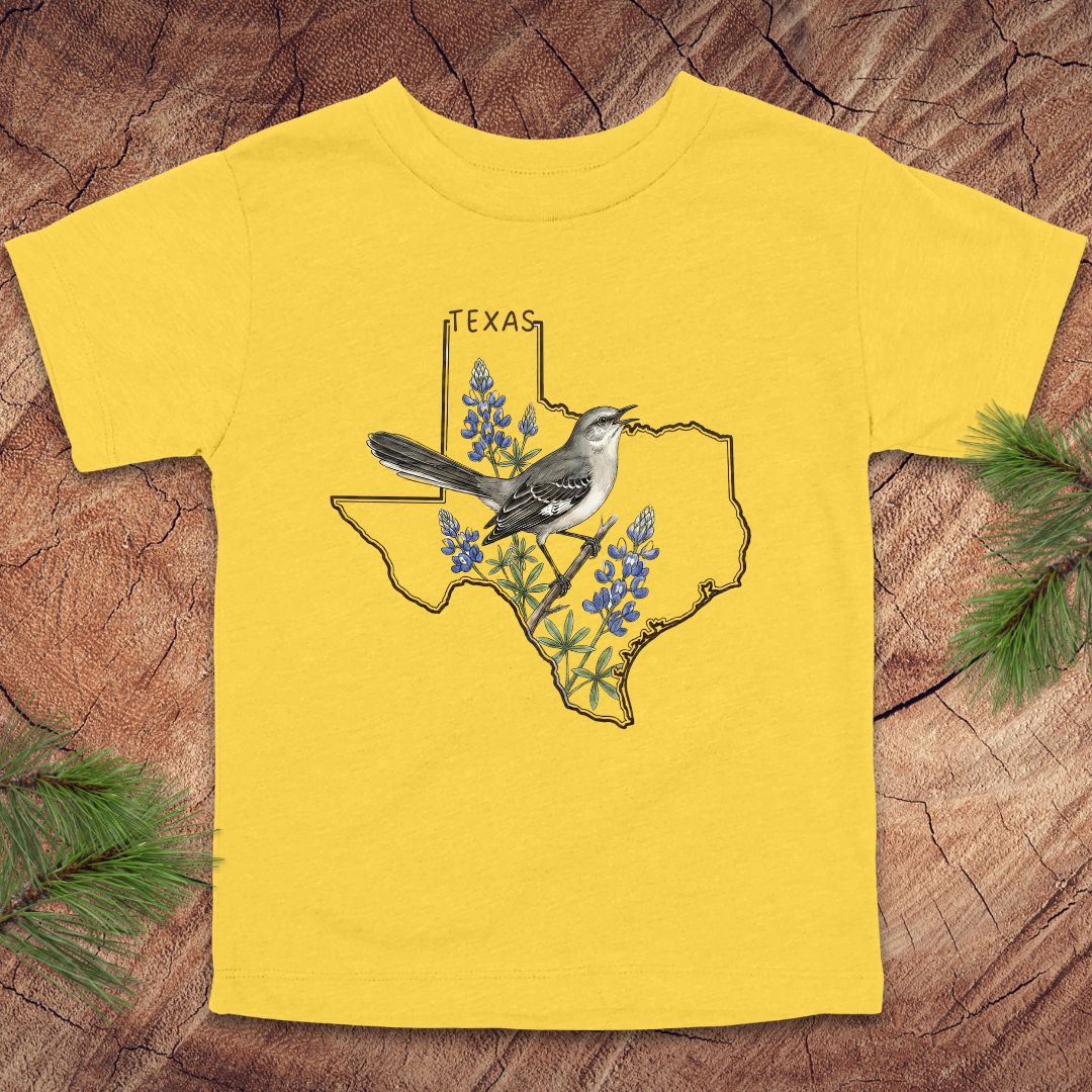 Yellow toddler t-shirt with Texas state outline and mockingbird on a wood background.