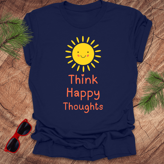 Navy blue t-shirt with a sun and 'Think Happy Thoughts' text on a wooden surface with sunglasses and greenery.