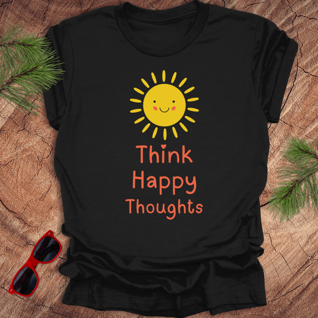 Black t-shirt with a sun and 'Think Happy Thoughts' text on a wooden surface with sunglasses and pine branches.