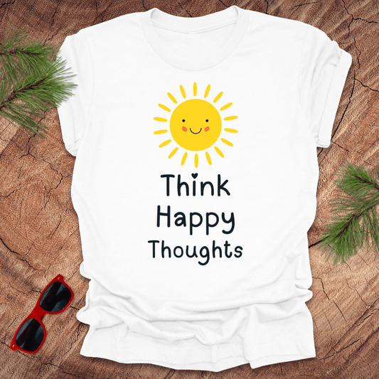 White t-shirt with a sun graphic and 'Think Happy Thoughts' text on a wooden surface with sunglasses and greenery.