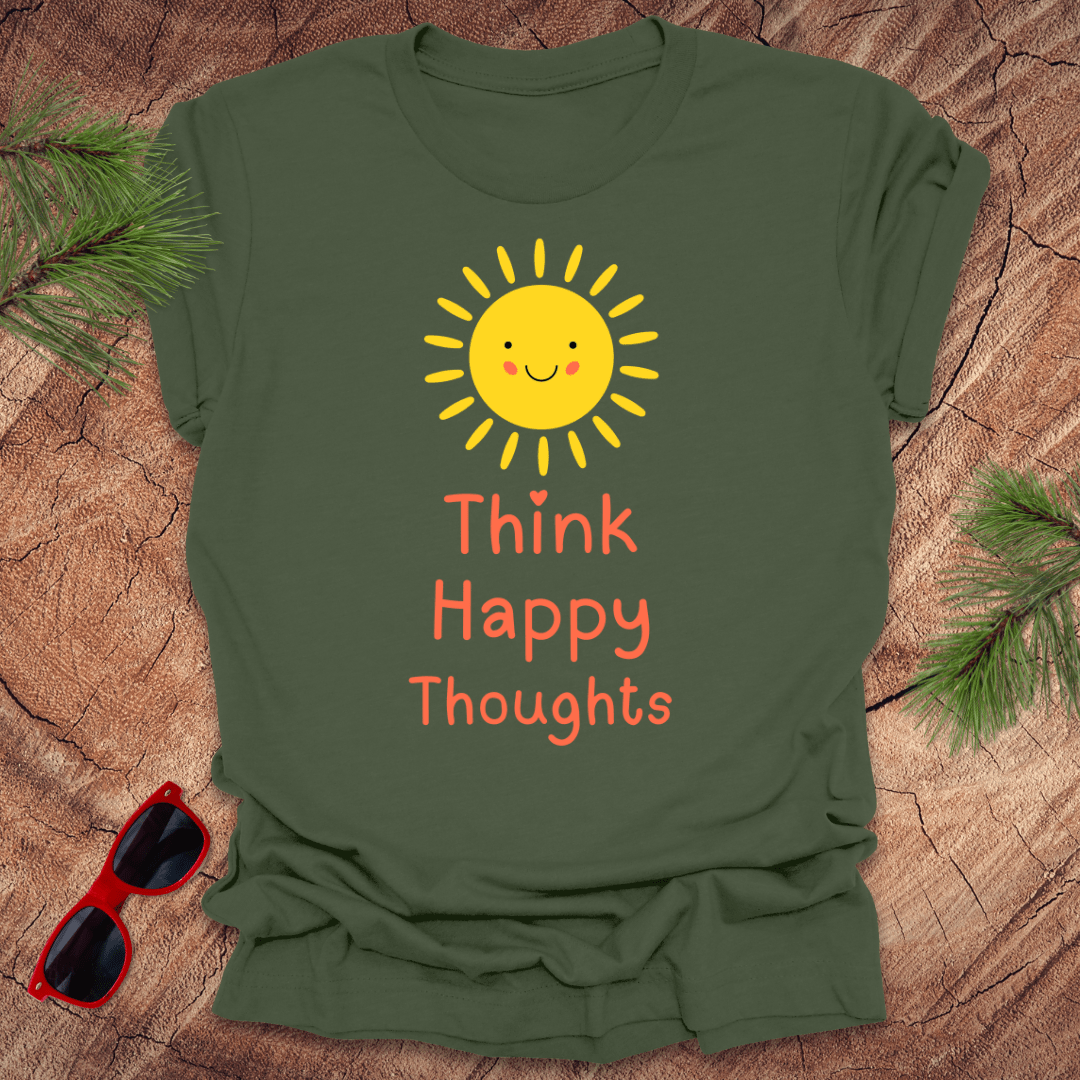 Green t-shirt with a sun and 'Think Happy Thoughts' text on a wooden surface with sunglasses and pine branches.