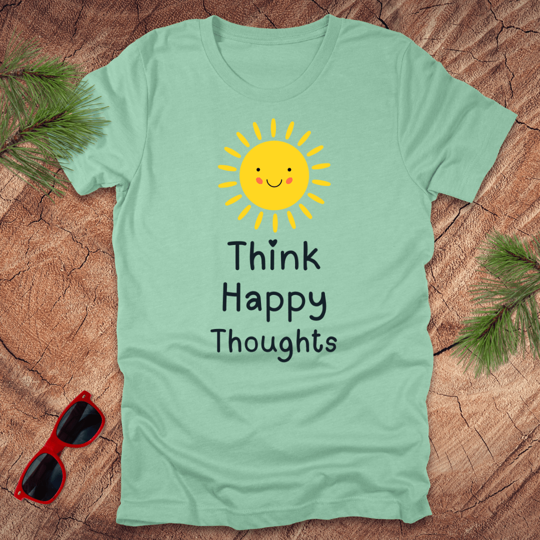 Light green t-shirt with a sun and text 'Think Happy Thoughts' on a wooden surface with sunglasses and foliage.