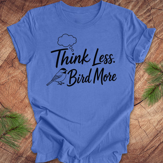 Blue t-shirt with 'Think Less. Bird More' text on a wooden surface