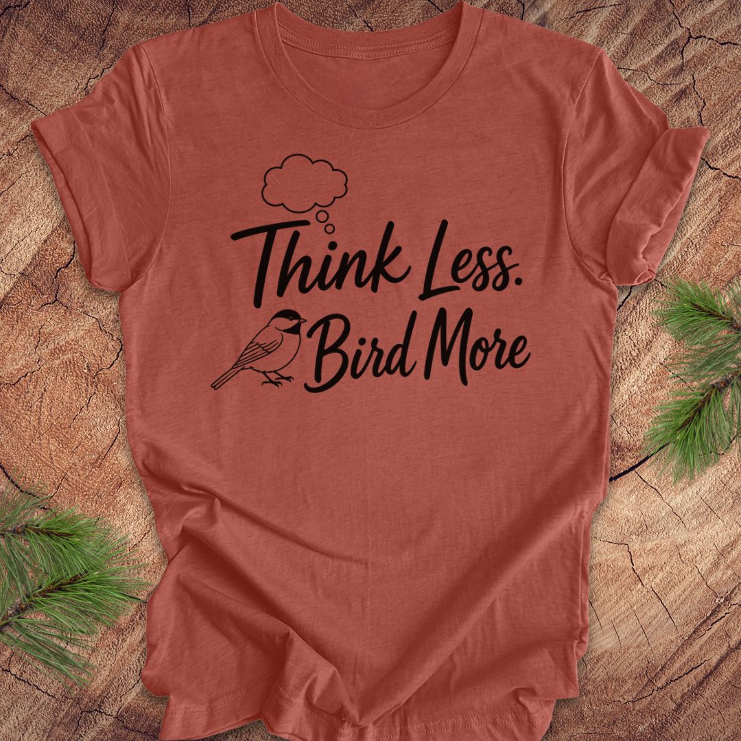 Red t-shirt with 'Think Less. Bird More' text on a wooden surface