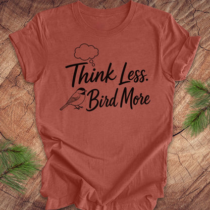 Red t-shirt with 'Think Less. Bird More' text on a wooden surface