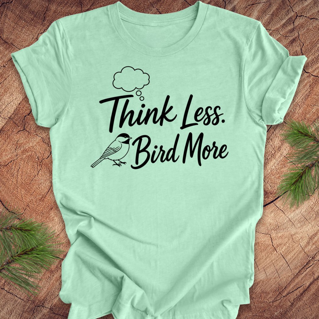 Light green t-shirt with 'Think Less Bird More' text on a wooden surface