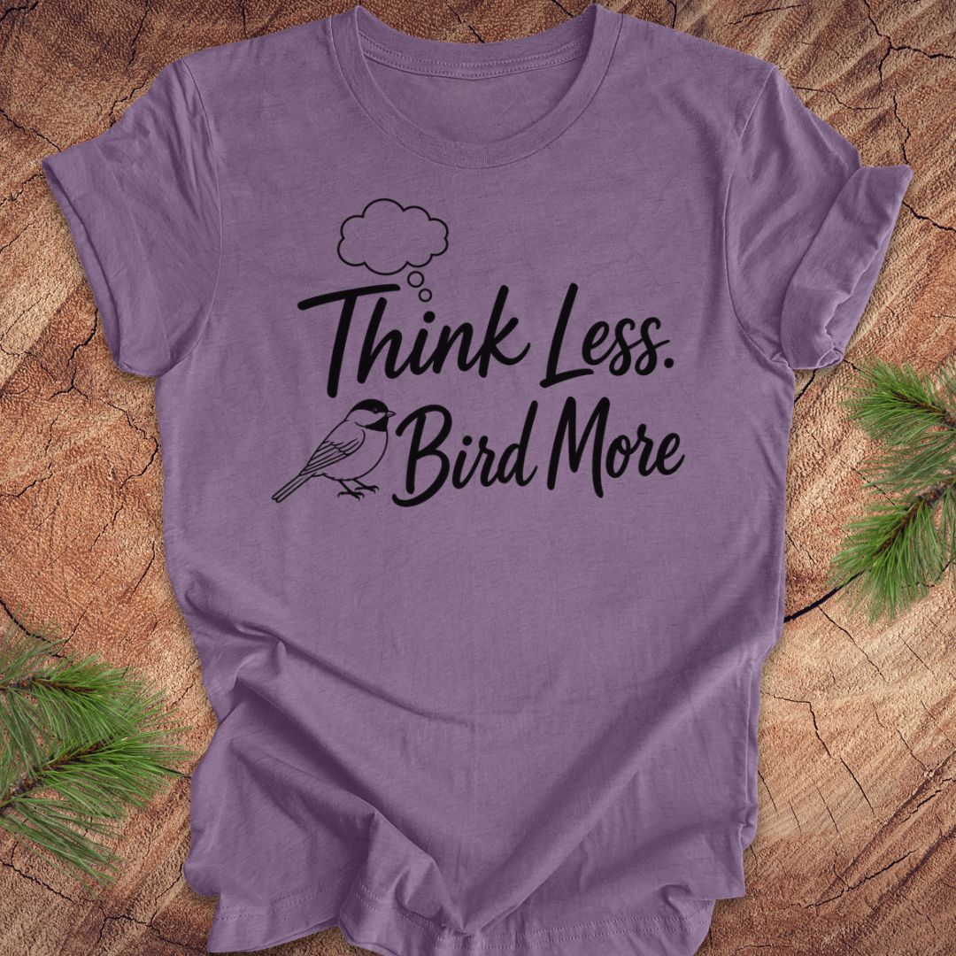 Purple t-shirt with 'Think Less. Bird More' text on a wooden surface