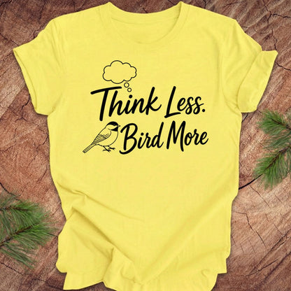 Yellow t-shirt with 'Think Less. Bird More' text on a wooden surface