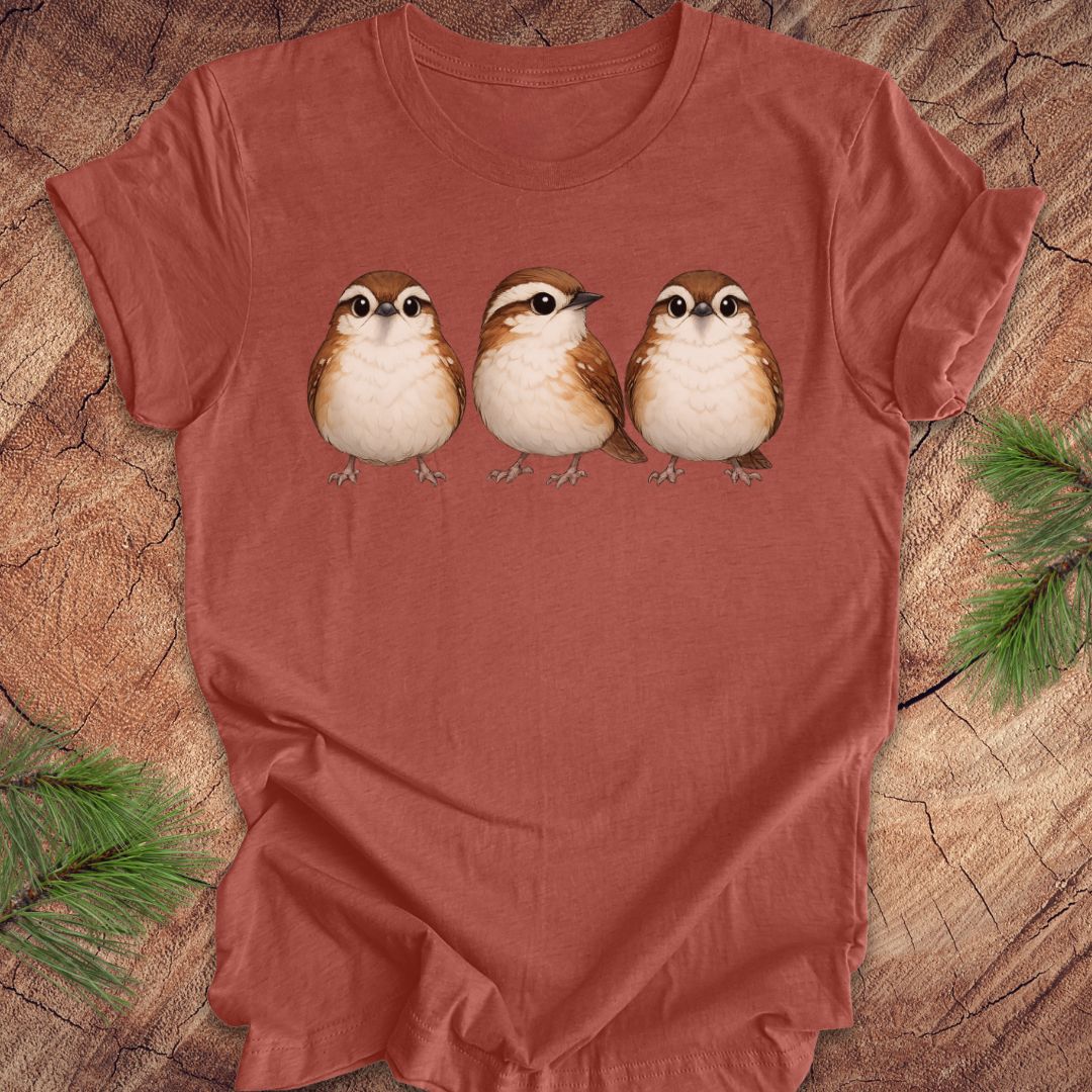 Clay colored t-shirt with three carolina wren birds on a wooden surface