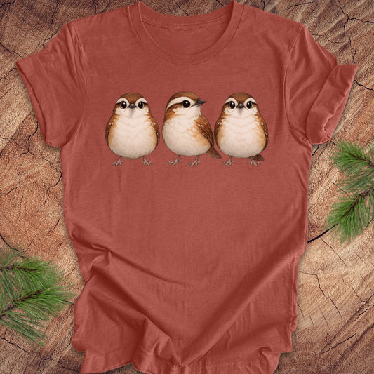 Clay colored t-shirt with three carolina wren birds on a wooden surface