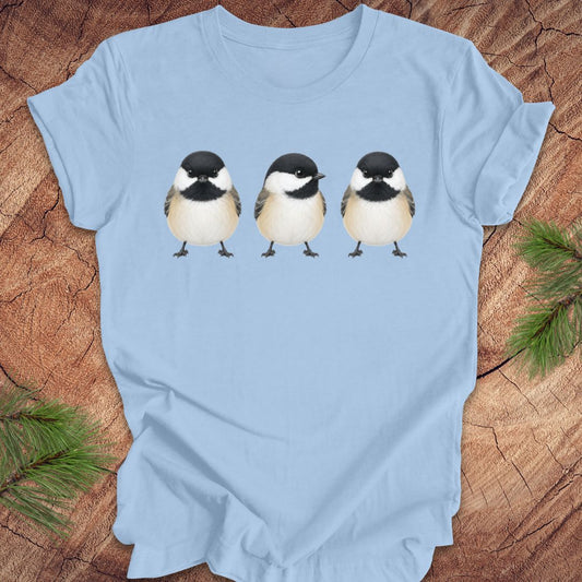 Light blue t-shirt with three chickadee illustrations on a wooden surface.