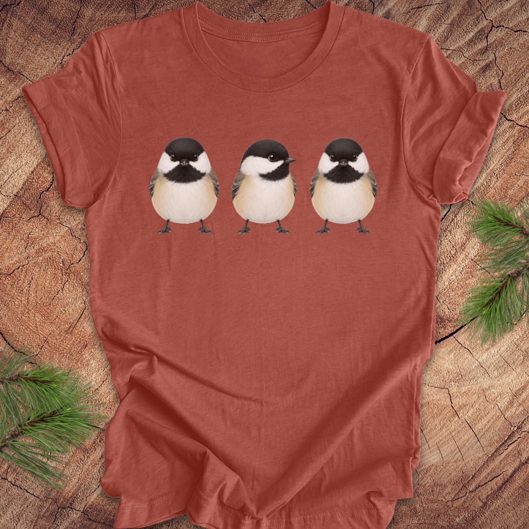 Red t-shirt with three chickadee illustrations on a wooden surface.