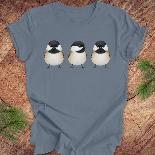 Blue t-shirt with three chickadee illustrations on a wooden surface.
