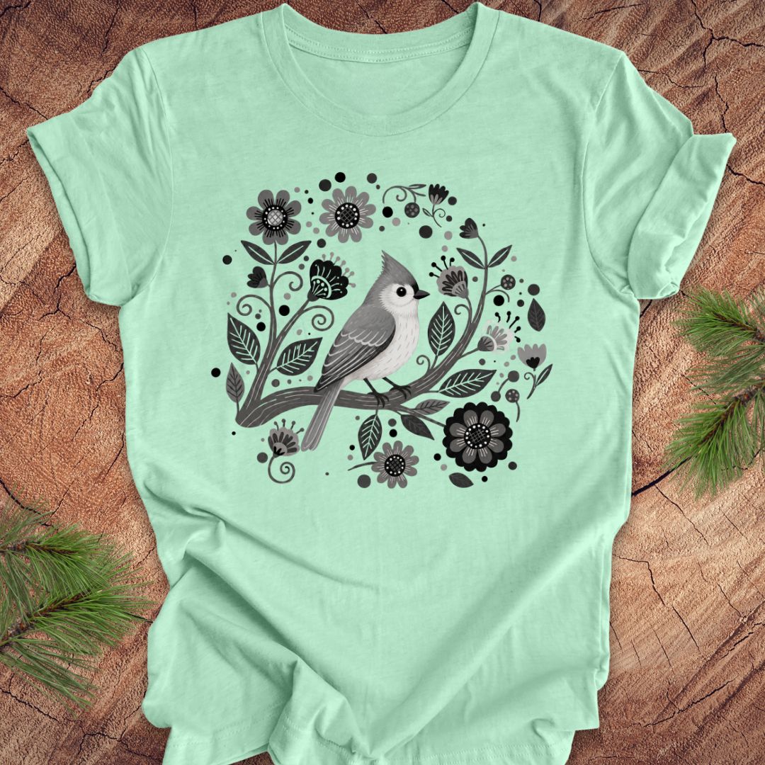 Mint green t-shirt with a titmouse bird and floral design on a wooden surface