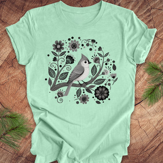 Mint green t-shirt with a titmouse bird and floral design on a wooden surface