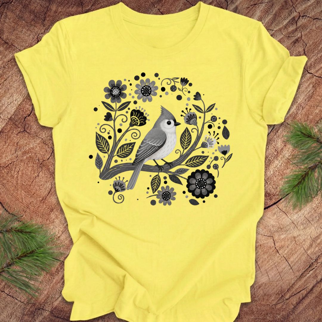 Yellow t-shirt with a titmouse bird and floral design on a wooden surface
