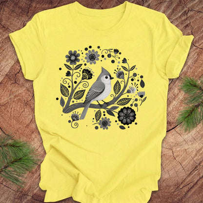 Yellow t-shirt with a titmouse bird and floral design on a wooden surface