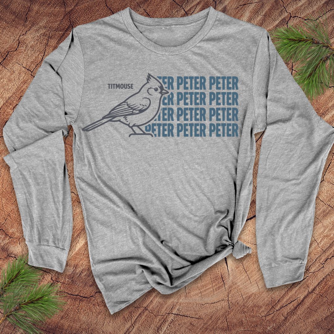 Gray long-sleeve shirt with a titmouse bird graphic and text on a wooden surface