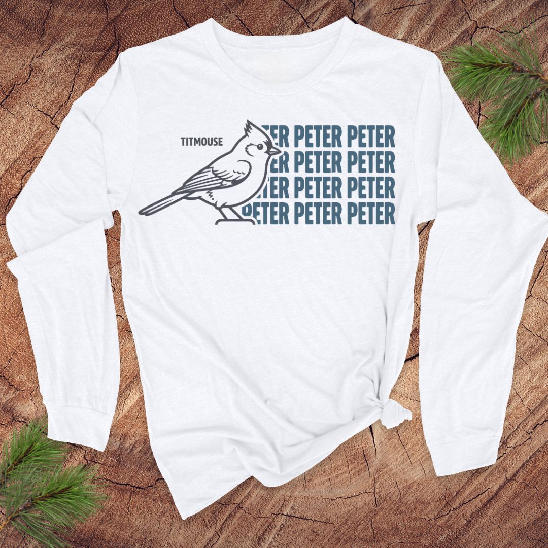 White long-sleeve shirt with titmouse bird graphic and text on a wooden surface