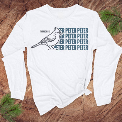 White long-sleeve shirt with titmouse bird graphic and text on a wooden surface