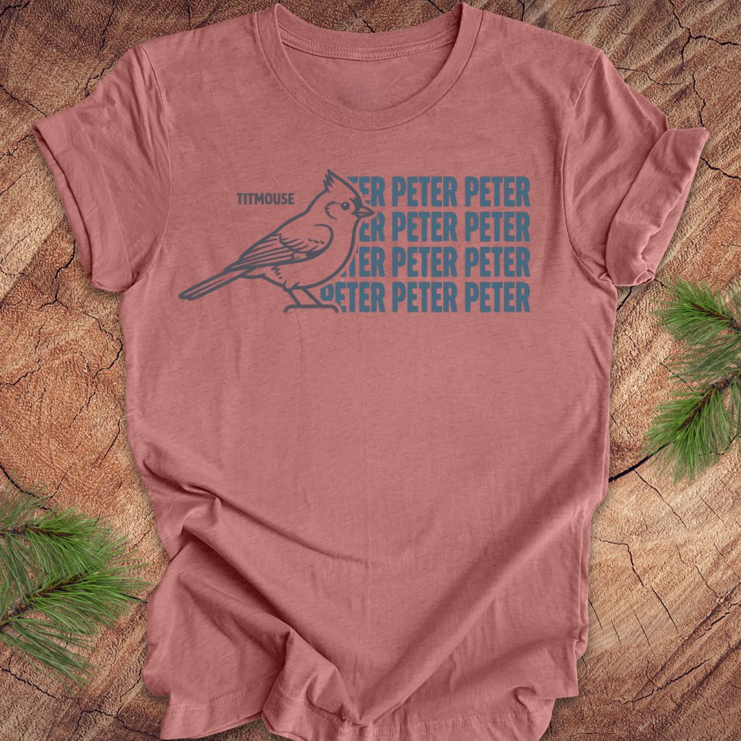 Mauve t-shirt with titmouse bird graphic and 'Peter Peter' text on a wooden surface