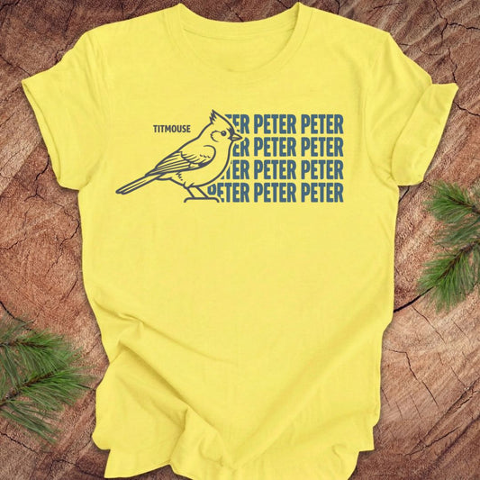 Yellow t-shirt with titmouse bird graphic and 'Peter Peter' text on a wooden surface