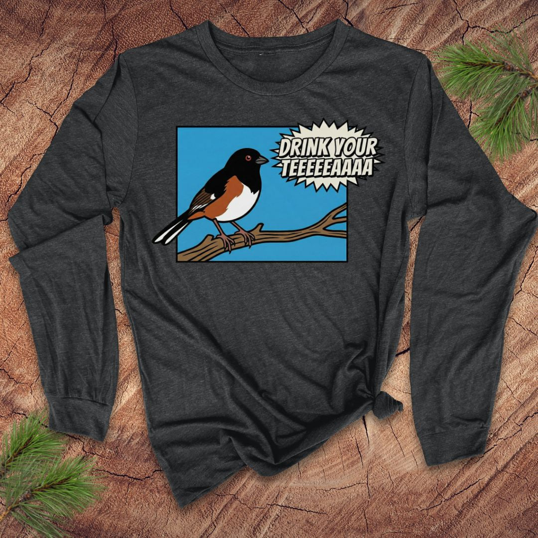 Dark gray long-sleeve shirt with a towhee bird graphic and text, 'drink your tea' on a wooden surface.