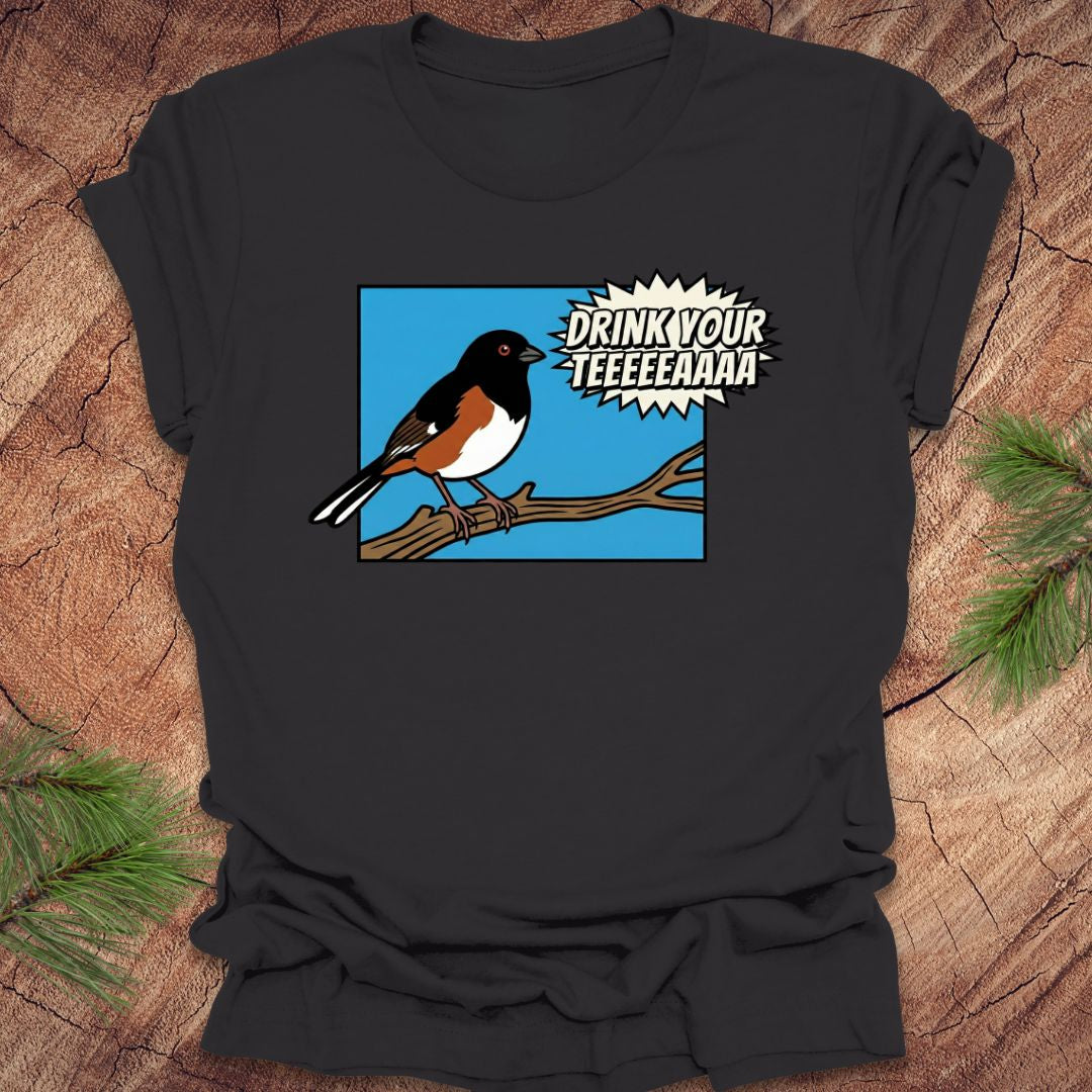 Dark gray t-shirt with a cartoon towhee bird graphic and text, 'drink your teeeaaa" on a wooden surface.