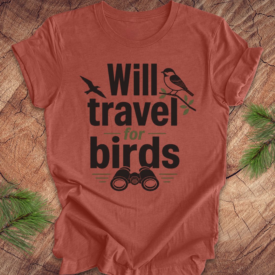 Clay colored t-shirt with text, 'will travel for birds' on a wood background. 