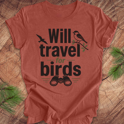 Clay colored t-shirt with text, 'will travel for birds' on a wood background. 