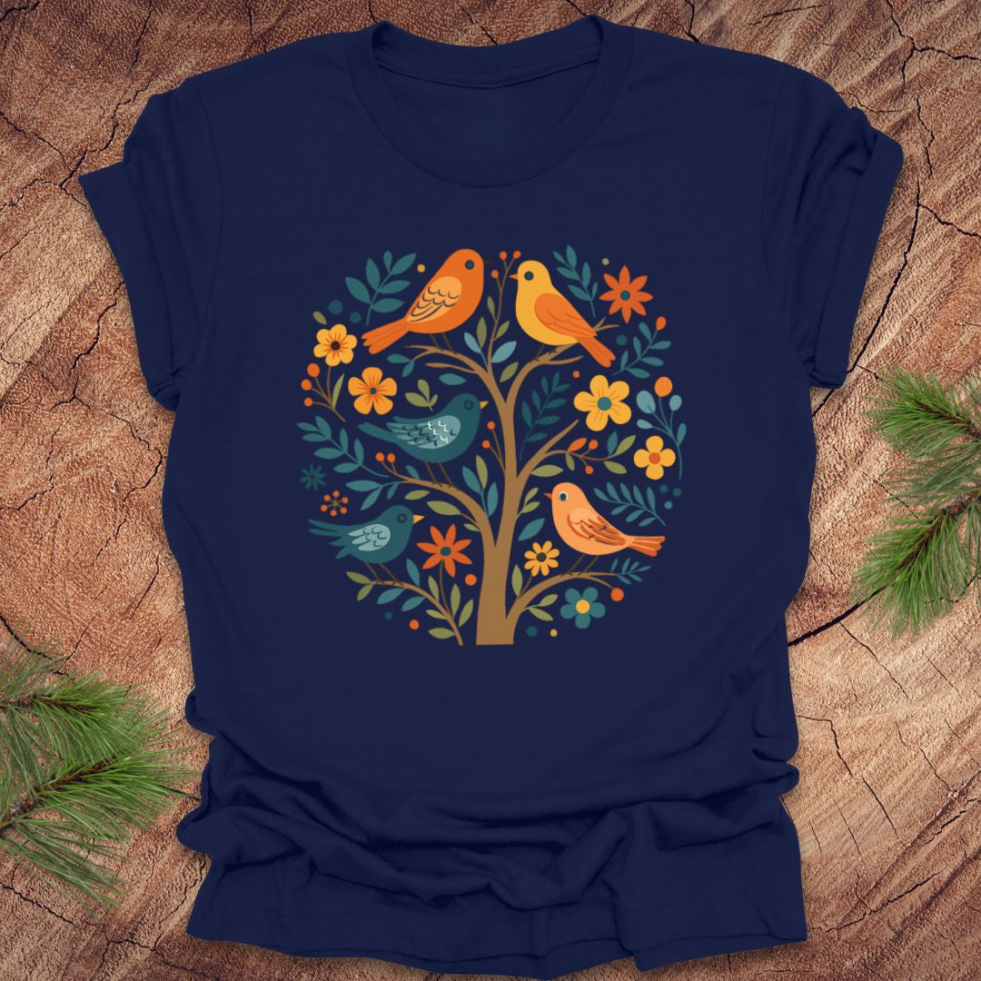 Navy blue t-shirt with colorful bird and tree design on a wooden surface with sunglasses and pine branches.