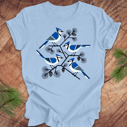 Baby blue t-shirt with geometric blue jay and tree design, on a wood background.
