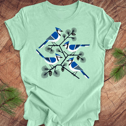 Mint green t-shirt with geometric blue jay and tree design, on a wood background.