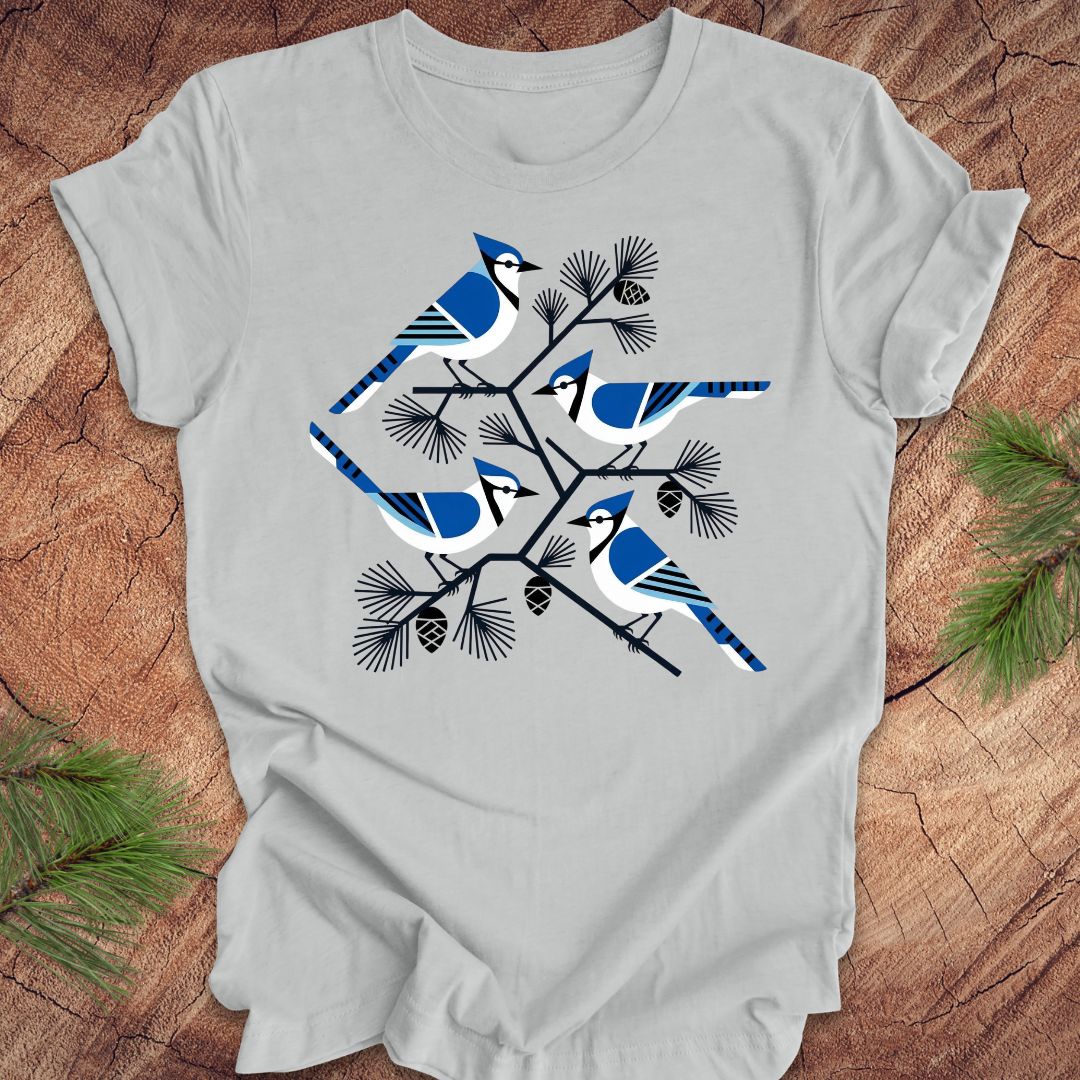 Silver t-shirt with geometric blue jay and tree design, on a wood background.