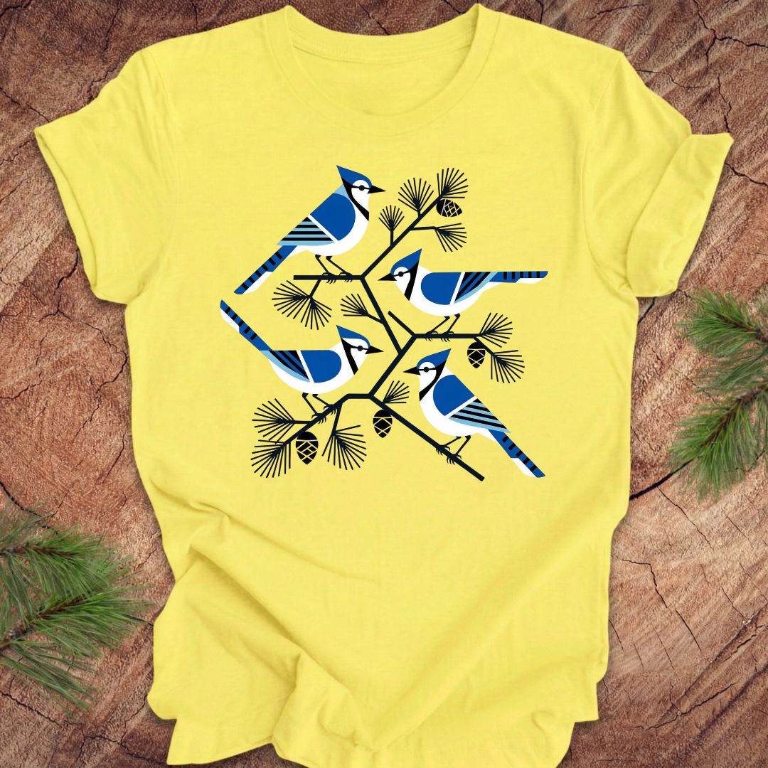 Yellow t-shirt with geometric blue jay and tree design, on a wood background.