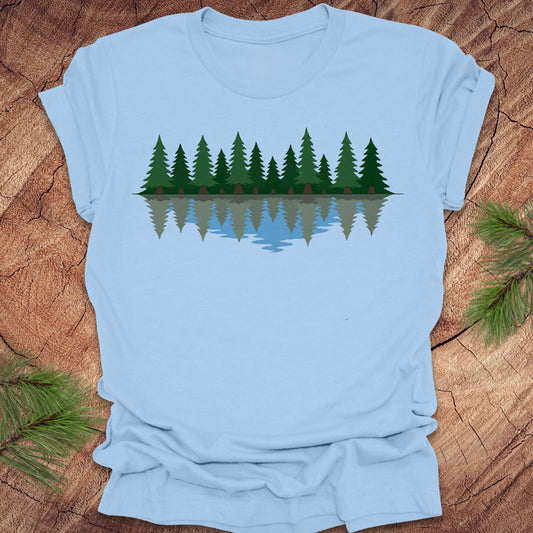 Light blue t-shirt with a graphic of trees reflected in water on a wooden surface.