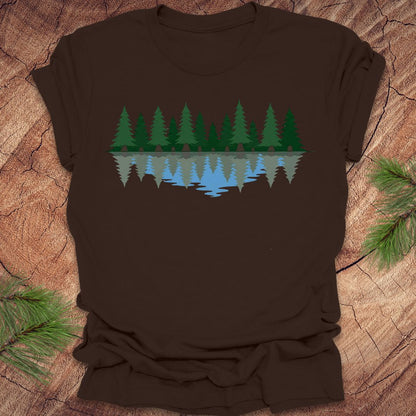 Brown t-shirt with a nature graphic of trees and water on a wooden surface.