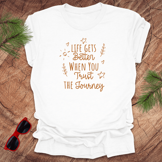 white tshirt with text life gets better when you trust the journey, on a wood background