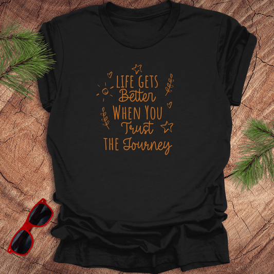 black tshirt with text life gets better when you trust the journey, on a wood background