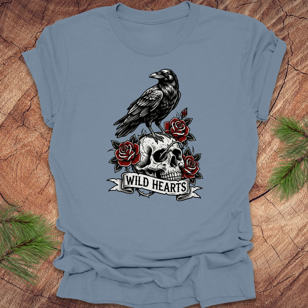 Blue t-shirt with a crow, skull, and roses design with text, 'wild hearts' on a wooden surface.