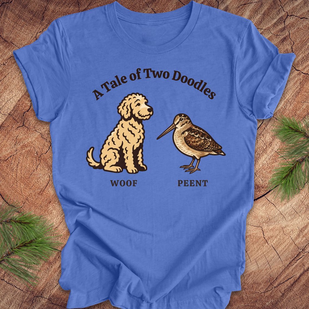 Blue t-shirt with a doodle dog and a woodcock bird with text, 'a tale of two doodles' on a wood background.