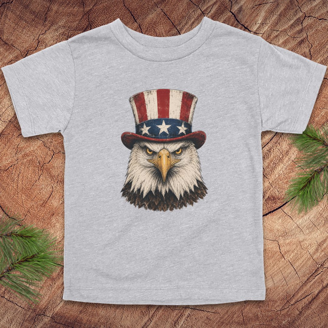 Gray toddler t-shirt with an eagle wearing a top hat on a wooden surface