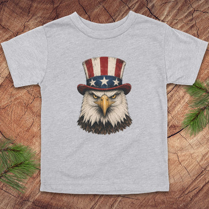 Gray toddler t-shirt with an eagle wearing a top hat on a wooden surface