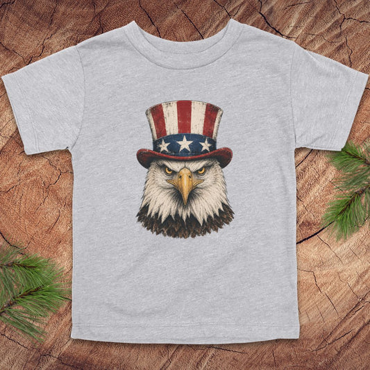 Gray toddler t-shirt with an eagle wearing a top hat on a wooden surface