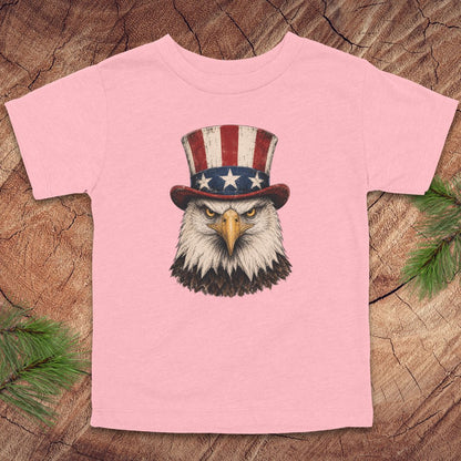 Pink toddler t-shirt with an eagle wearing a top hat on a wooden surface