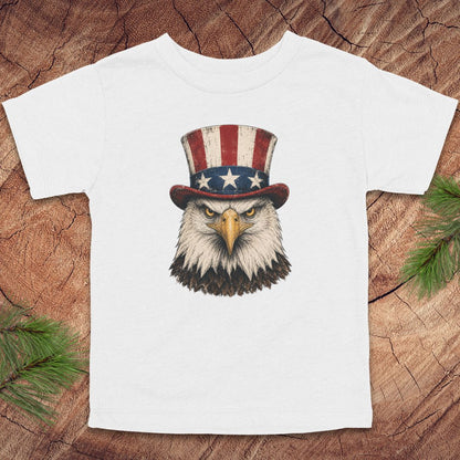 White toddler t-shirt with an eagle wearing a top hat on a wooden surface