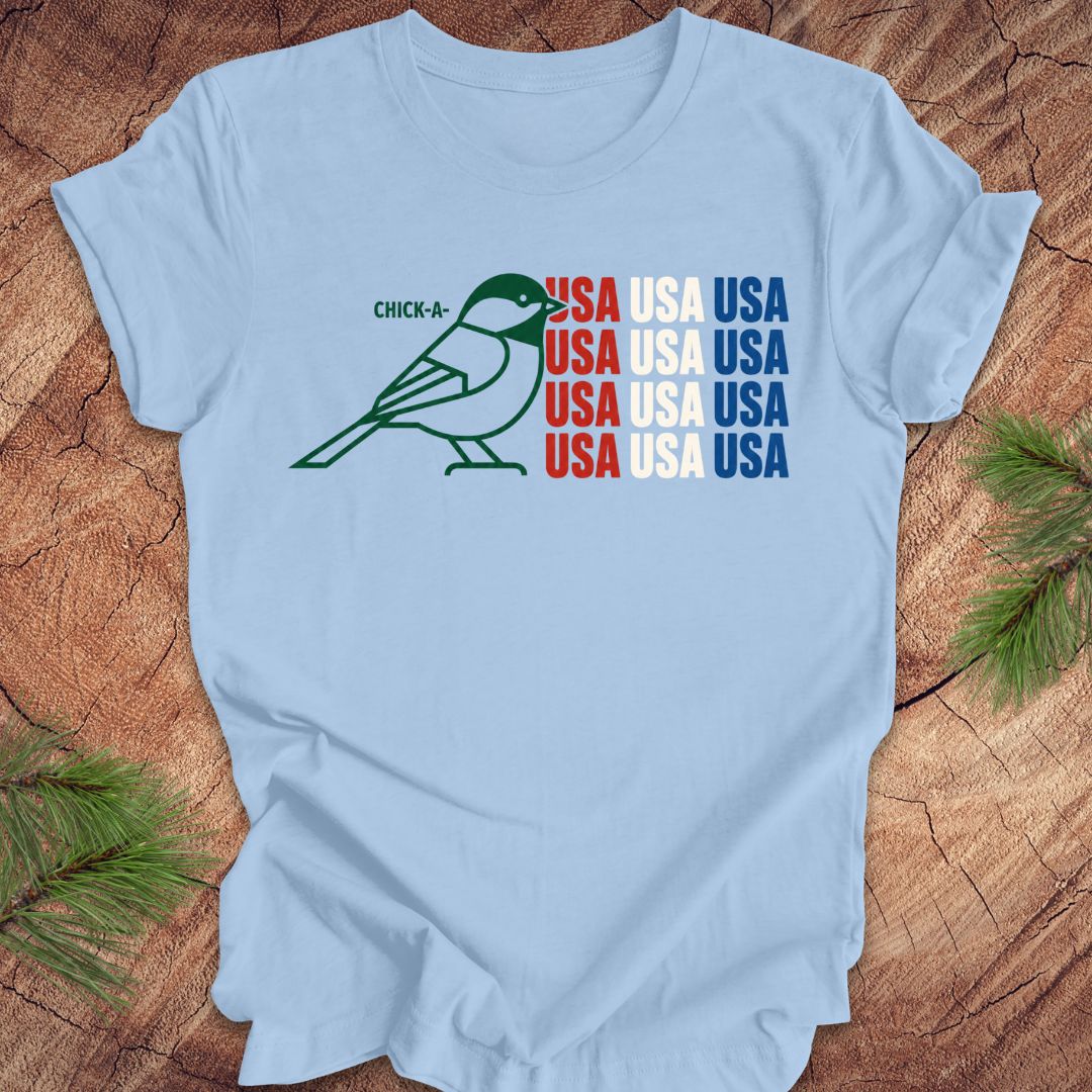 Light blue t-shirt with a chickadee bird graphic and 'USA' text on a wooden surface.