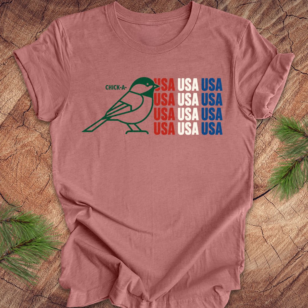 Mauve t-shirt with a chickadee bird graphic and 'USA' text on a wooden surface.