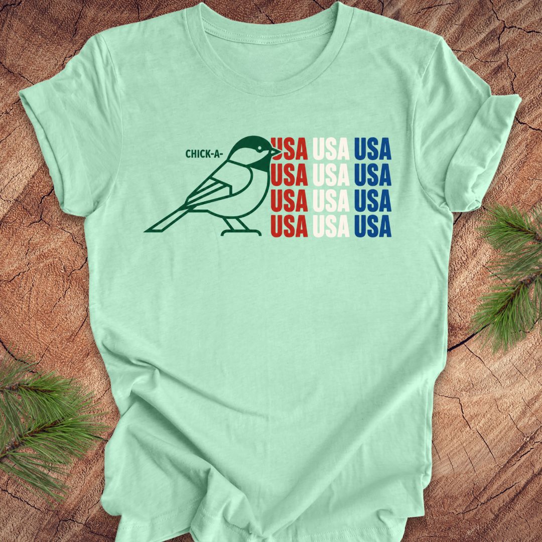 Mint green t-shirt with a chickadee bird graphic and 'USA' text on a wooden surface.