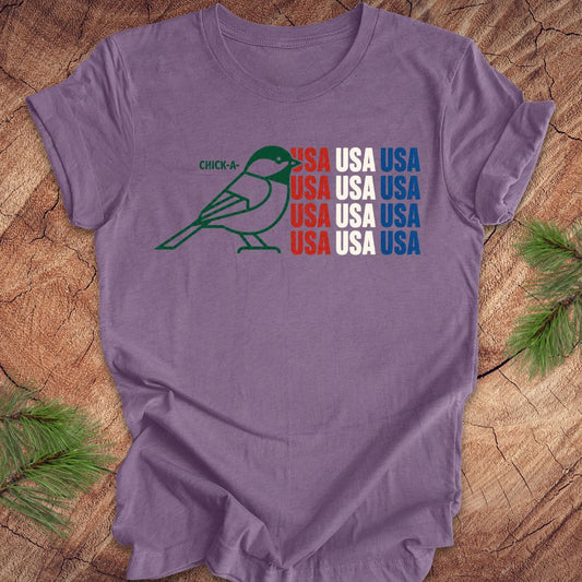 Purple t-shirt with a chickadee bird graphic and 'USA' text on a wooden surface.